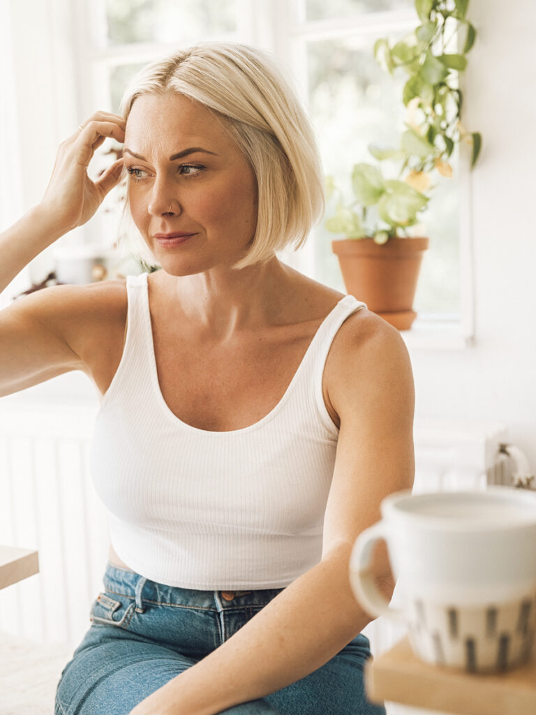 Woman at home indoors by her kitchen table drinking coffee